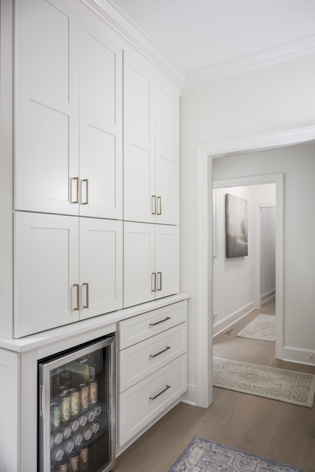 Built-in beverage refrigerator and full-height white cabinetry with brass hardware